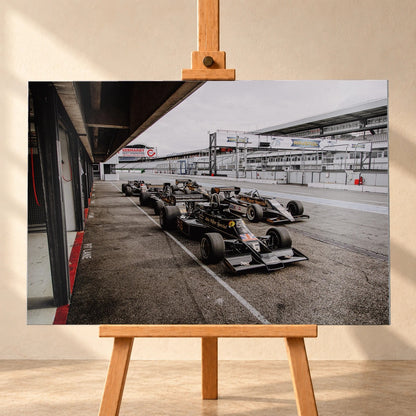 Mehrere historische Lotus-Rennwagen rollen in enger Formation an der Boxengasse entlang; der Blick von oben zeigt die Staffelung. Motiv „Trackside Moment“ als Alu gebürstet-Wandbild, frontal auf einer Holzstaffelei.