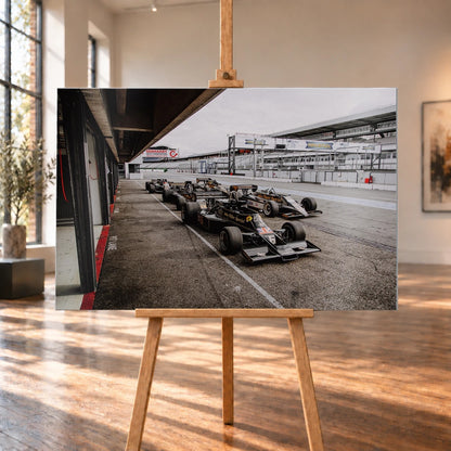 Mehrere historische Lotus-Rennwagen rollen in enger Formation an der Boxengasse entlang; der Blick von oben zeigt die Staffelung. Motiv „Trackside Moment“ als Alu gebürstet-Wandbild, auf einer Holzstaffelei in einem hellen Galerieraum.