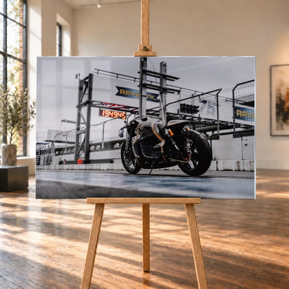 Raumvisualisierung eines querformatigen Acrylglasbilds mit dem schwarz-goldenen Lotus C-01 in einer Boxengasse. Das Bild steht auf einer Holzstaffelei im hellen Raum mit hohen Fenstern; Fensterreflexionen überlagern den linken Motivbereich.