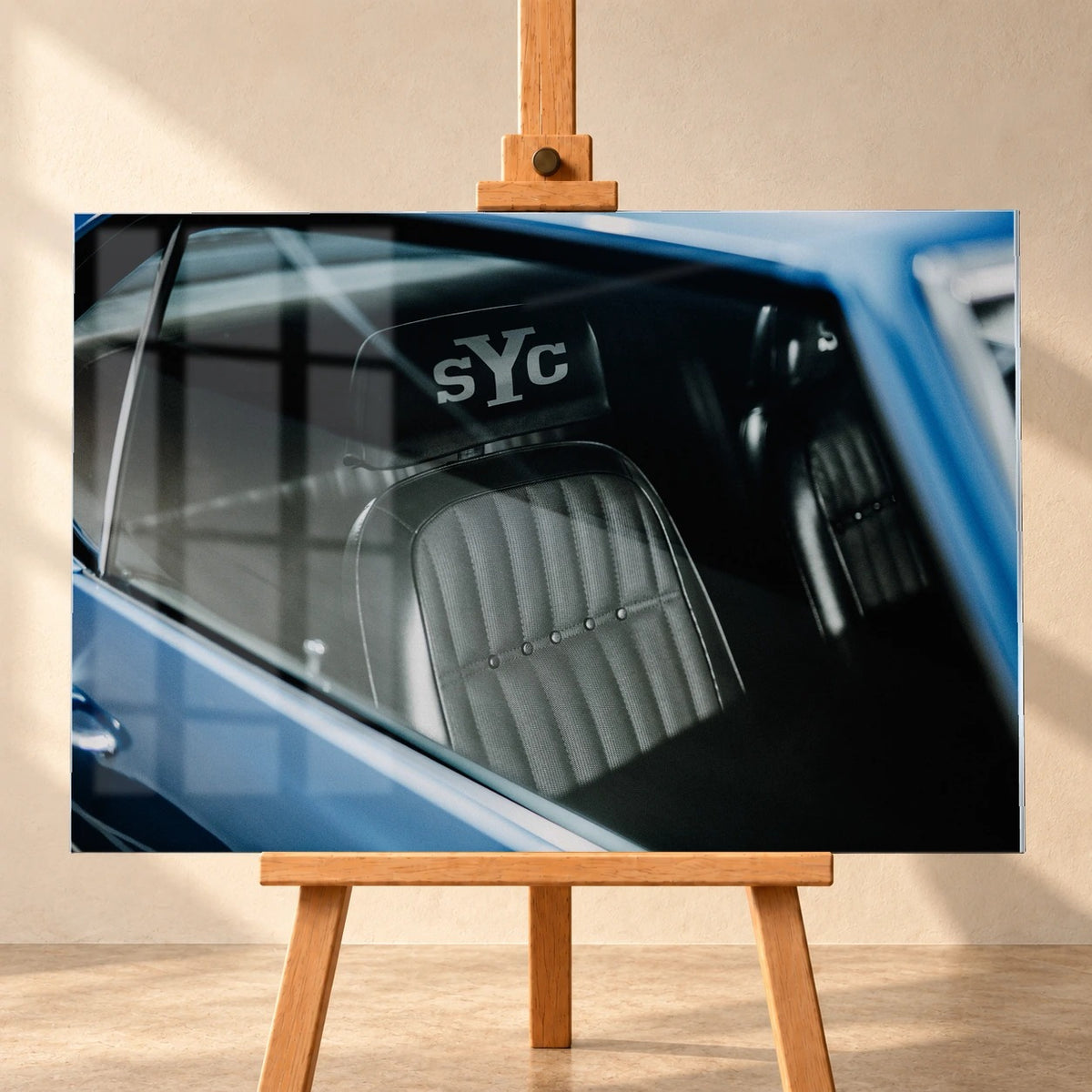 Die Innenraum-Nahaufnahme des blauen Camaro Yenko zeigt den hellen Sitz mit SYC-Schriftzug, eingefasst von Fenster und Karosserie. Motiv „Hero Moment 2“ als Acrylglas-Wandbild, frontal auf einer Holzstaffelei.