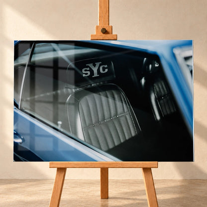 Die Innenraum-Nahaufnahme des blauen Camaro Yenko zeigt den hellen Sitz mit SYC-Schriftzug, eingefasst von Fenster und Karosserie. Motiv „Hero Moment 2“ als Acrylglas-Wandbild, frontal auf einer Holzstaffelei.
