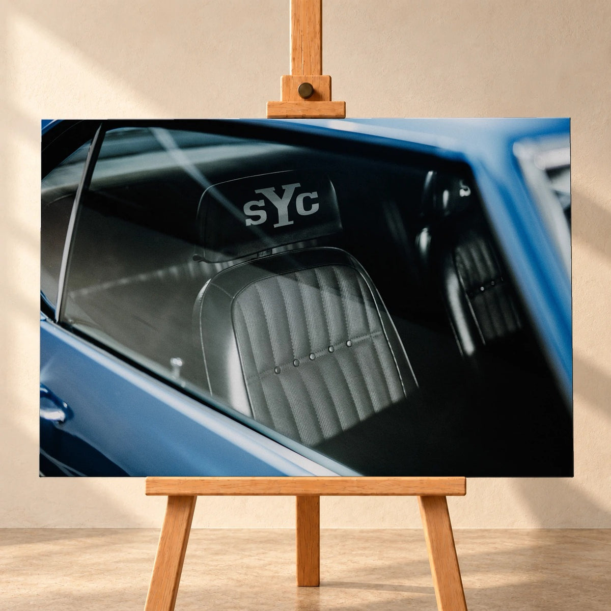 Die Innenraum-Nahaufnahme des blauen Camaro Yenko zeigt den hellen Sitz mit SYC-Schriftzug, eingefasst von Fenster und Karosserie. Motiv „Hero Moment 2“ als Leinwand-Wandbild, frontal auf einer Holzstaffelei.