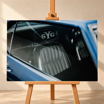 Die Innenraum-Nahaufnahme des blauen Camaro Yenko zeigt den hellen Sitz mit SYC-Schriftzug, eingefasst von Fenster und Karosserie. Motiv „Hero Moment 2“ als Leinwand-Wandbild, frontal auf einer Holzstaffelei.
