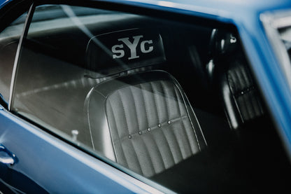 Die Innenraum-Nahaufnahme des blauen Camaro Yenko zeigt den hellen Sitz mit SYC-Schriftzug, eingefasst von Fenster und Karosserie. Originalmotiv „Hero Moment 2“ im Querformat.