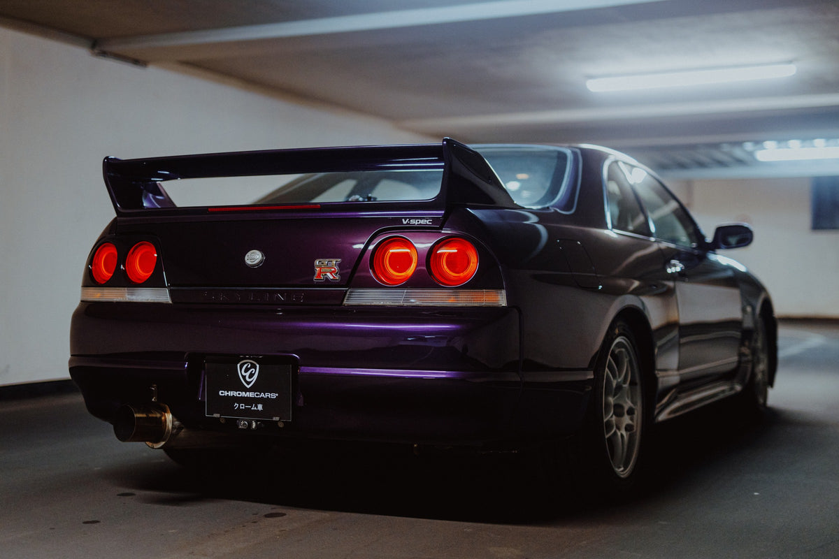 Der Nissan Skyline R33 steht schräg von hinten in einer Parkhauskurve; Rundlichter und Spoiler heben sich vom kühlen Beton ab. Originalmotiv „Neon Story“ im Querformat.