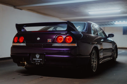 Der Nissan Skyline R33 steht schräg von hinten in einer Parkhauskurve; Rundlichter und Spoiler heben sich vom kühlen Beton ab. Originalmotiv „Neon Story“ im Querformat.