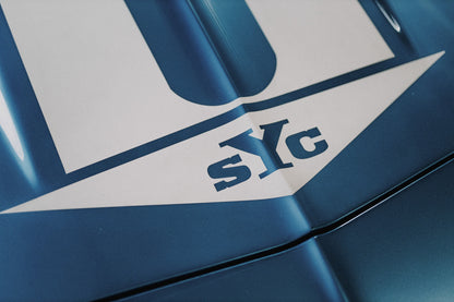 Die Nahaufnahme zeigt weiße Haubenstreifen und großen SYC-Schriftzug auf dem blauen Camaro Yenko. Originalmotiv „Urban Light 2“ im Querformat.