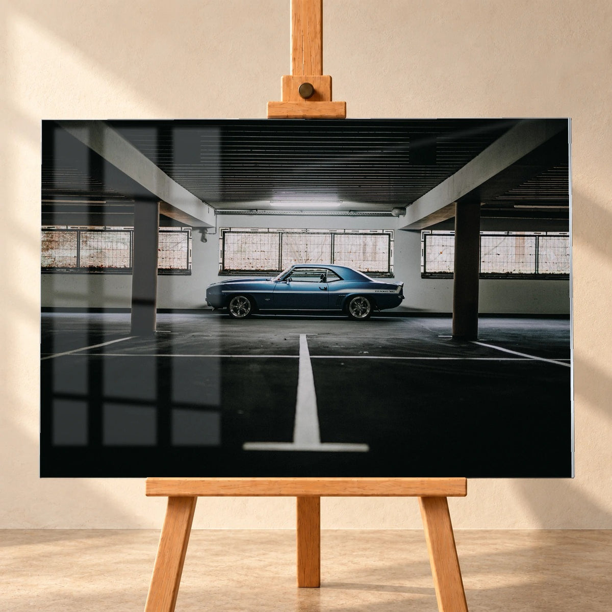 Der Camaro Yenko steht klein im Seitenprofil in einer großen, dunklen Industriehalle; helle Bodenmarkierung und Fensterlicht rahmen ihn ein. Motiv „Road Line“ als Acrylglas-Wandbild, frontal auf einer Holzstaffelei.