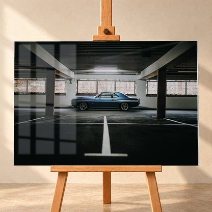 Der Camaro Yenko steht klein im Seitenprofil in einer großen, dunklen Industriehalle; helle Bodenmarkierung und Fensterlicht rahmen ihn ein. Motiv „Road Line“ als Acrylglas-Wandbild, frontal auf einer Holzstaffelei.