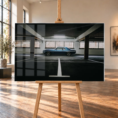 Der Camaro Yenko steht klein im Seitenprofil in einer großen, dunklen Industriehalle; helle Bodenmarkierung und Fensterlicht rahmen ihn ein. Motiv „Road Line“ als Acrylglas-Wandbild, auf einer Holzstaffelei in einem hellen Galerieraum.