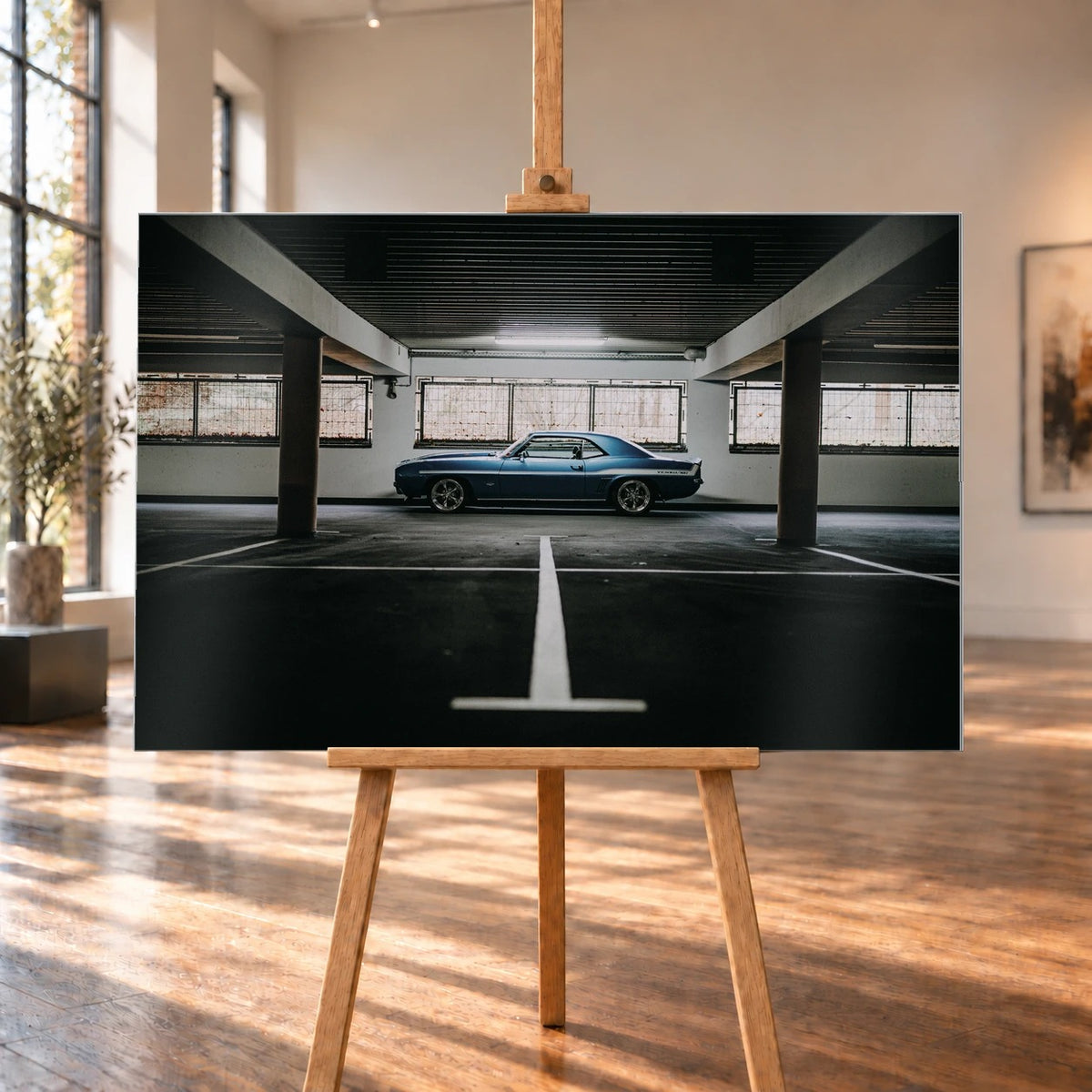 Der Camaro Yenko steht klein im Seitenprofil in einer großen, dunklen Industriehalle; helle Bodenmarkierung und Fensterlicht rahmen ihn ein. Motiv „Road Line“ als Alu gebürstet-Wandbild, auf einer Holzstaffelei in einem hellen Galerieraum.