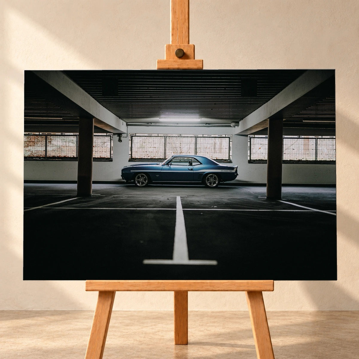 Der Camaro Yenko steht klein im Seitenprofil in einer großen, dunklen Industriehalle; helle Bodenmarkierung und Fensterlicht rahmen ihn ein. Motiv „Road Line“ als Leinwand-Wandbild, frontal auf einer Holzstaffelei.