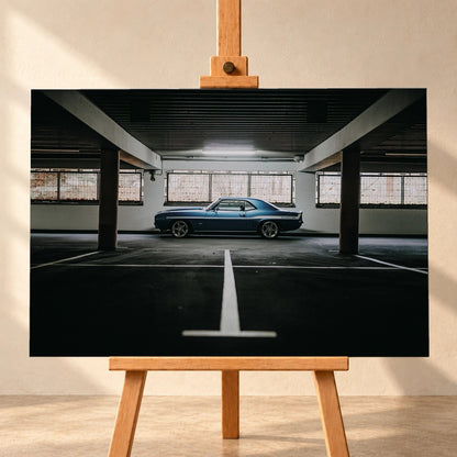 Der Camaro Yenko steht klein im Seitenprofil in einer großen, dunklen Industriehalle; helle Bodenmarkierung und Fensterlicht rahmen ihn ein. Motiv „Road Line“ als Leinwand-Wandbild, frontal auf einer Holzstaffelei.