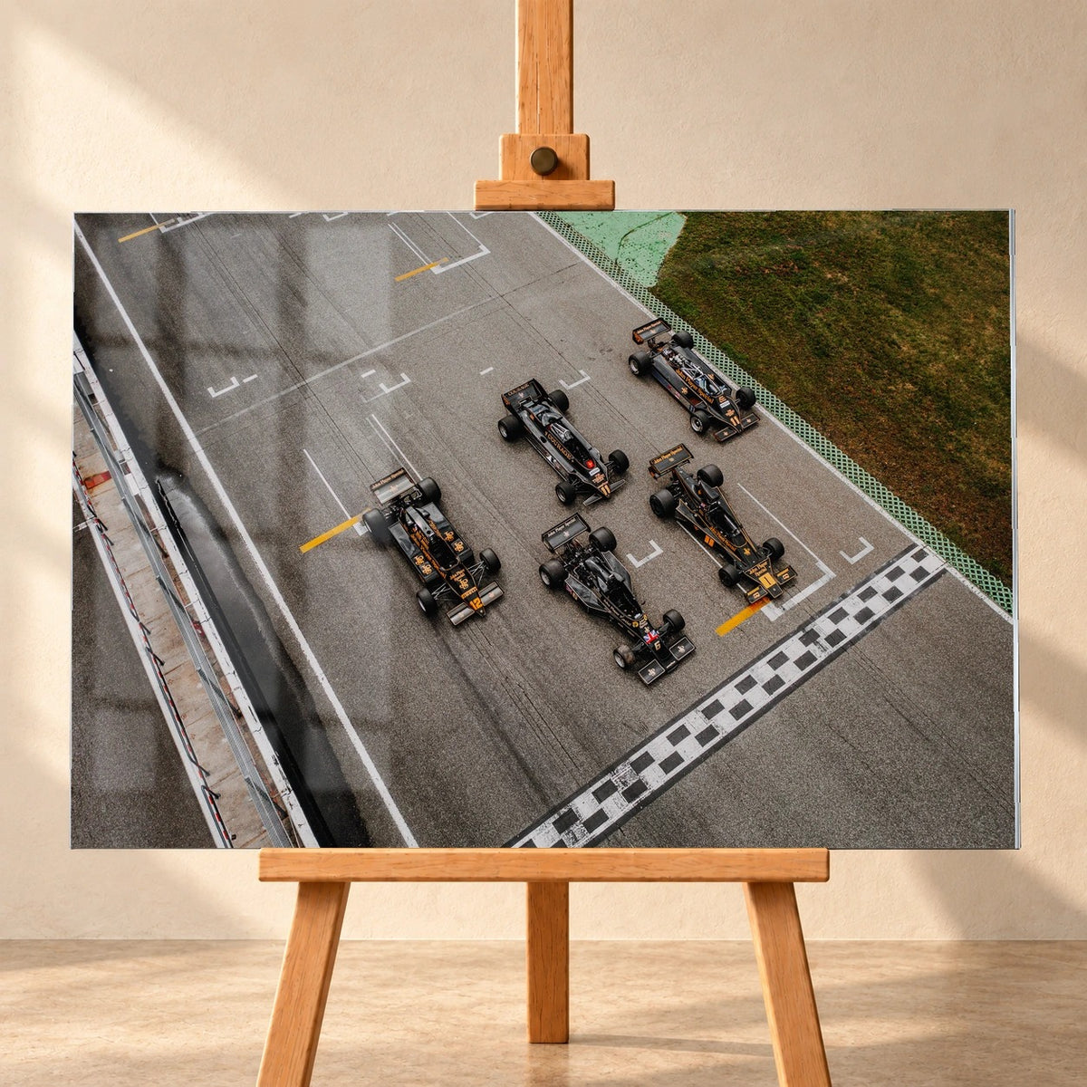 Fünf Lotus-Formelwagen stehen aus der Vogelperspektive nebeneinander auf der Startlinie; Markierungen und Asphalt erzeugen ein grafisches Raster. Motiv „Velocity Story“ als Acrylglas-Wandbild, frontal auf einer Holzstaffelei.