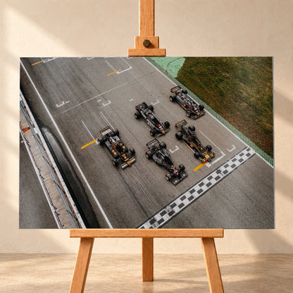 Fünf Lotus-Formelwagen stehen aus der Vogelperspektive nebeneinander auf der Startlinie; Markierungen und Asphalt erzeugen ein grafisches Raster. Motiv „Velocity Story“ als Alu gebürstet-Wandbild, frontal auf einer Holzstaffelei.