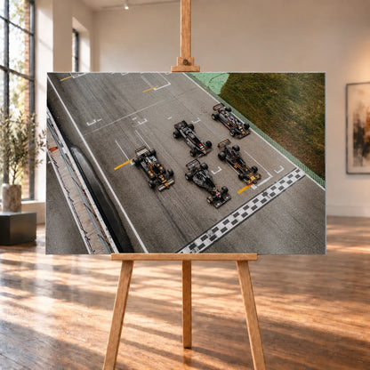 Fünf Lotus-Formelwagen stehen aus der Vogelperspektive nebeneinander auf der Startlinie; Markierungen und Asphalt erzeugen ein grafisches Raster. Motiv „Velocity Story“ als Alu gebürstet-Wandbild, auf einer Holzstaffelei in einem hellen Galerieraum.