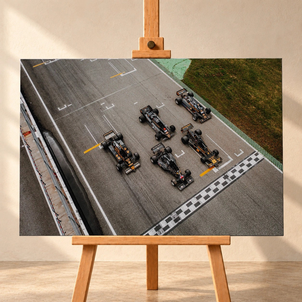 Fünf Lotus-Formelwagen stehen aus der Vogelperspektive nebeneinander auf der Startlinie; Markierungen und Asphalt erzeugen ein grafisches Raster. Motiv „Velocity Story“ als Leinwand-Wandbild, frontal auf einer Holzstaffelei.