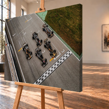 Fünf Lotus-Formelwagen stehen aus der Vogelperspektive nebeneinander auf der Startlinie; Markierungen und Asphalt erzeugen ein grafisches Raster. Motiv „Velocity Story“ als Leinwand-Wandbild, schräg von der Seite auf einer Holzstaffelei.