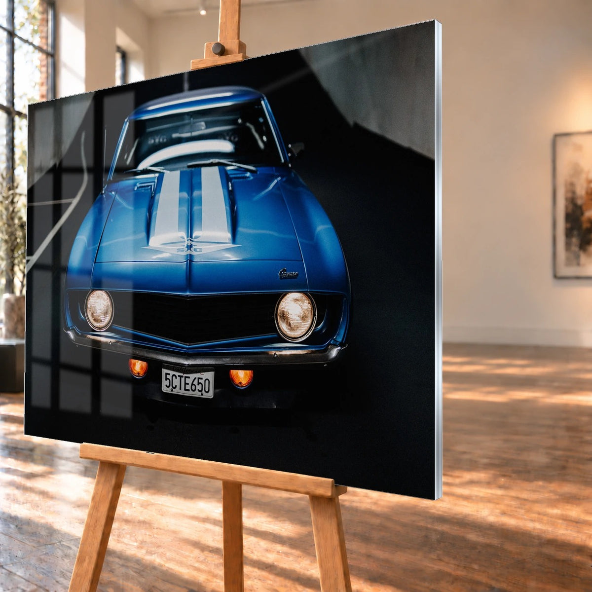 Der Camaro Yenko ist frontal und symmetrisch aufgenommen; blaue Haube, weiße Doppelstreifen und runde Scheinwerfer stehen im Mittelpunkt. Motiv „Silver Horizon 2“ als Acrylglas-Wandbild, schräg von der Seite auf einer Holzstaffelei.