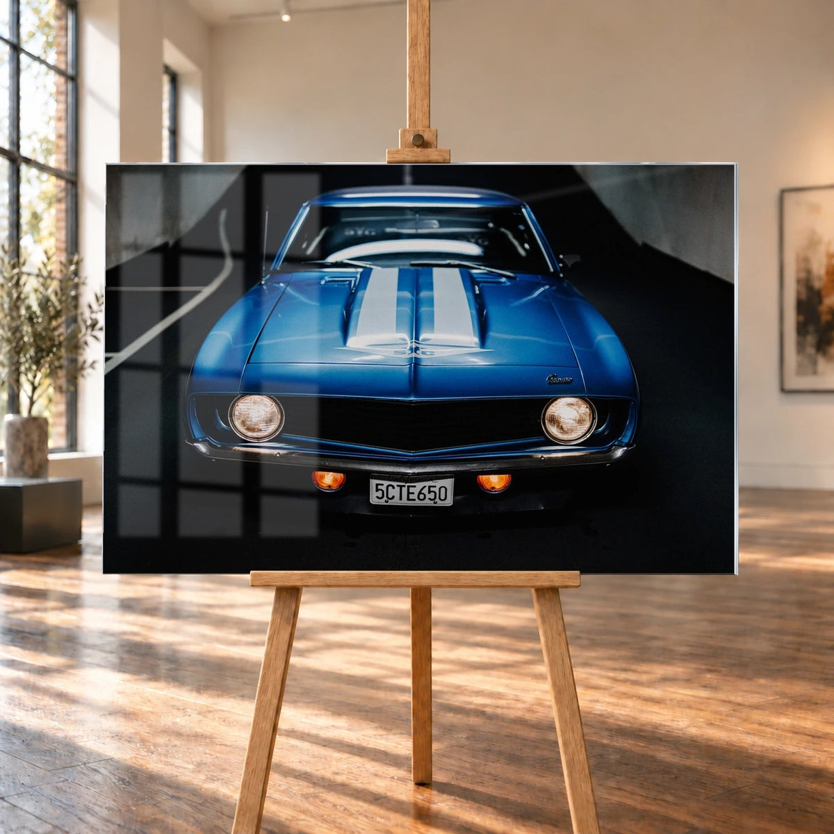 Der Camaro Yenko ist frontal und symmetrisch aufgenommen; blaue Haube, weiße Doppelstreifen und runde Scheinwerfer stehen im Mittelpunkt. Motiv „Silver Horizon 2“ als Acrylglas-Wandbild, auf einer Holzstaffelei in einem hellen Galerieraum.