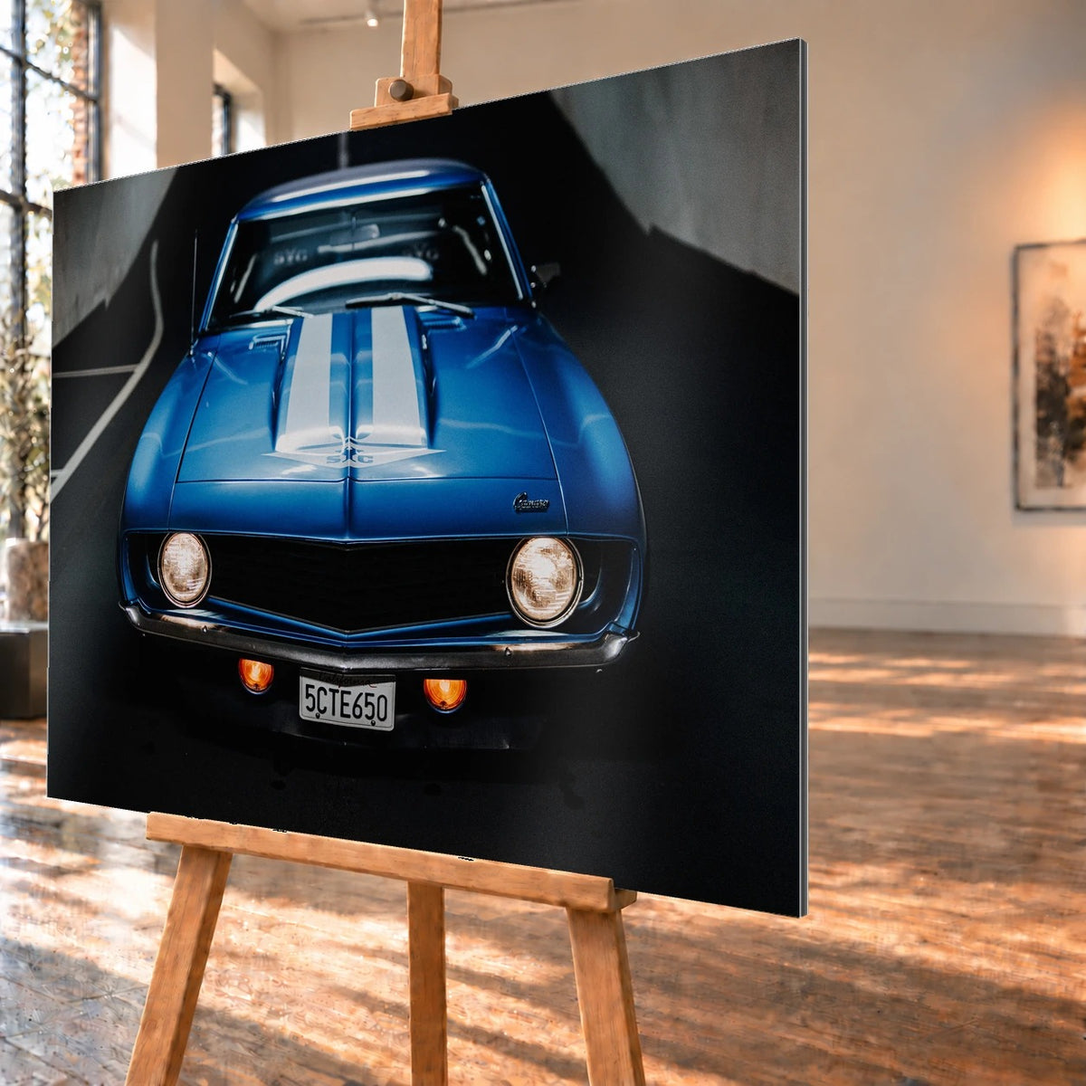 Der Camaro Yenko ist frontal und symmetrisch aufgenommen; blaue Haube, weiße Doppelstreifen und runde Scheinwerfer stehen im Mittelpunkt. Motiv „Silver Horizon 2“ als Alu gebürstet-Wandbild, schräg von der Seite auf einer Holzstaffelei.