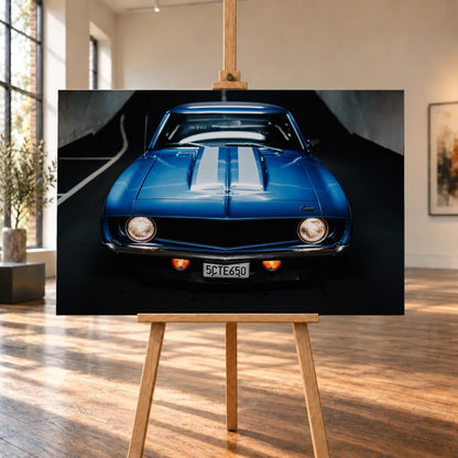Der Camaro Yenko ist frontal und symmetrisch aufgenommen; blaue Haube, weiße Doppelstreifen und runde Scheinwerfer stehen im Mittelpunkt. Motiv „Silver Horizon 2“ als Leinwand-Wandbild, auf einer Holzstaffelei in einem hellen Galerieraum.