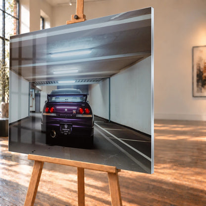 Der Nissan Skyline R33 steht mittig von hinten in einer leeren Parkhausachse; seine vier Rundlichter leuchten vor kühlem Beton. Motiv „Midnight Depth 2“ als Acrylglas-Wandbild, schräg von der Seite auf einer Holzstaffelei.