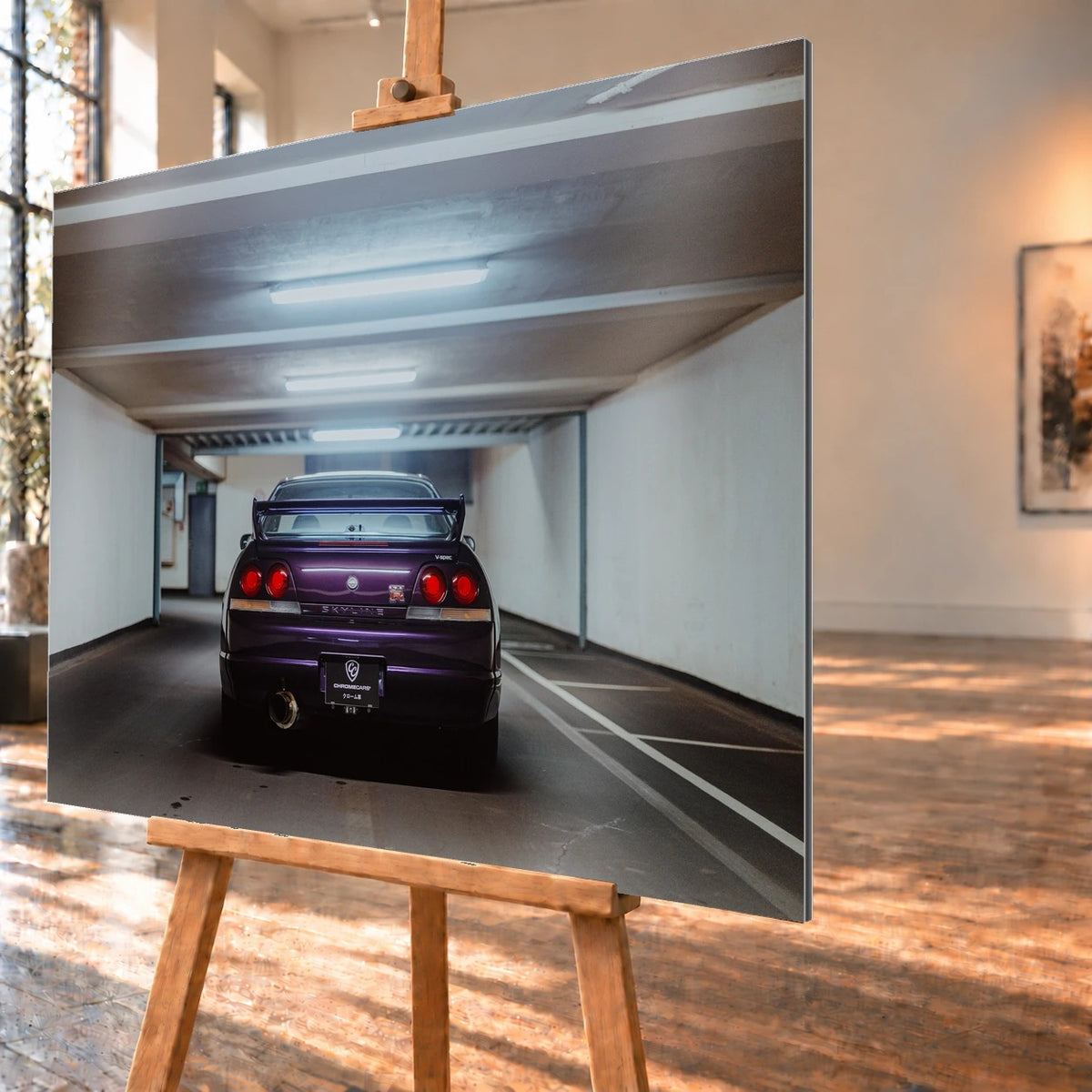 Der Nissan Skyline R33 steht mittig von hinten in einer leeren Parkhausachse; seine vier Rundlichter leuchten vor kühlem Beton. Motiv „Midnight Depth 2“ als Alu gebürstet-Wandbild, schräg von der Seite auf einer Holzstaffelei.