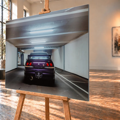 Der Nissan Skyline R33 steht mittig von hinten in einer leeren Parkhausachse; seine vier Rundlichter leuchten vor kühlem Beton. Motiv „Midnight Depth 2“ als Alu gebürstet-Wandbild, schräg von der Seite auf einer Holzstaffelei.