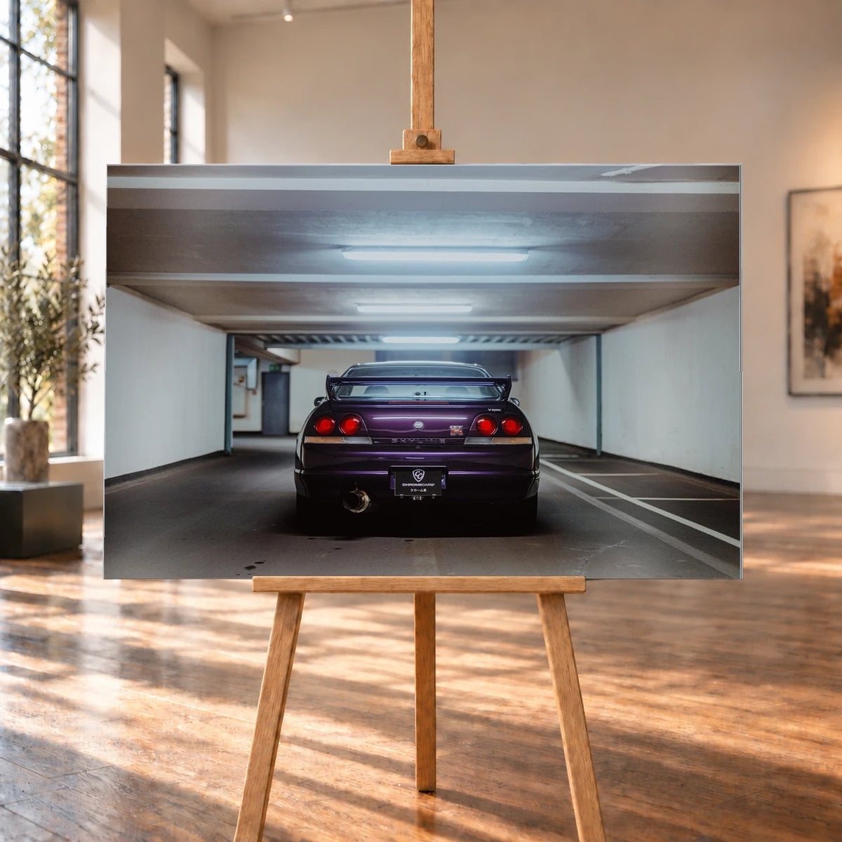 Der Nissan Skyline R33 steht mittig von hinten in einer leeren Parkhausachse; seine vier Rundlichter leuchten vor kühlem Beton. Motiv „Midnight Depth 2“ als Alu gebürstet-Wandbild, auf einer Holzstaffelei in einem hellen Galerieraum.