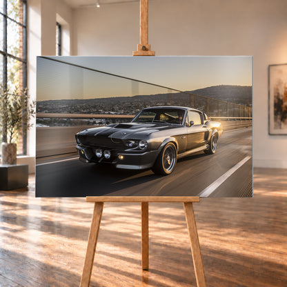 Grauer Eleanor-Sportwagen fährt im Abendlicht über eine Brücke, mit Stadt und Hügeln im Hintergrund; Visualisierung als Alu gebürstet-Wandbild, auf einer Holzstaffelei in einem hellen Galerieraum.
