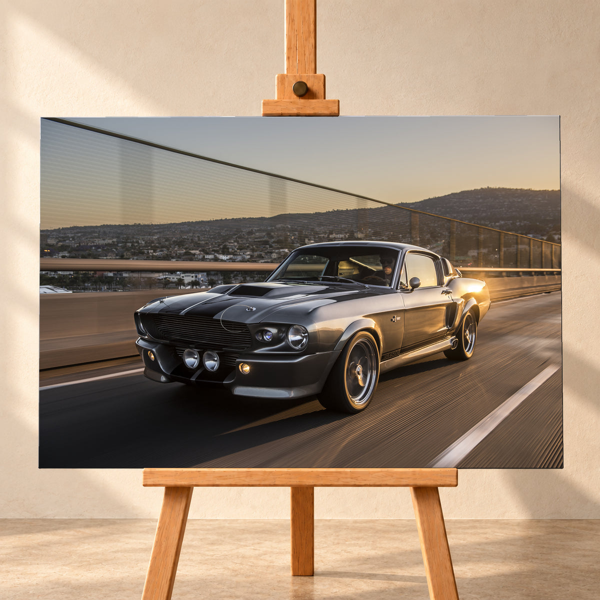 Grauer Eleanor-Sportwagen fährt im Abendlicht über eine Brücke, mit Stadt und Hügeln im Hintergrund; Visualisierung als Leinwand-Wandbild, frontal auf einer Holzstaffelei.