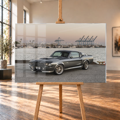 Dunkelgrauer Ford Mustang Shelby GT500 mit kontrastierenden Längsstreifen in Front-Dreiviertelansicht auf einer Hafenfläche; dahinter Wasser, Boote, Containerkräne, leuchtende Hafenlampen und ein pastellfarbener Abendhimmel; Visualisierung als Acrylglas-Wandbild, auf einer Holzstaffelei in einem hellen Galerieraum.