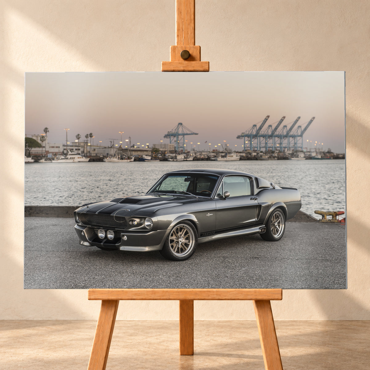 Dunkelgrauer Ford Mustang Shelby GT500 mit kontrastierenden Längsstreifen in Front-Dreiviertelansicht auf einer Hafenfläche; dahinter Wasser, Boote, Containerkräne, leuchtende Hafenlampen und ein pastellfarbener Abendhimmel; Visualisierung als Alu gebürstet-Wandbild, frontal auf einer Holzstaffelei.