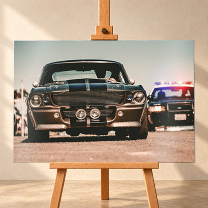Dunkler Eleanor Ford Mustang Shelby GT500 in tiefer Frontalansicht auf heller Fahrbahn, mit dunklen Längsstreifen, Motorhaubenaufsatz, Rundscheinwerfern und zwei Zusatzleuchten. Rechts dahinter steht unscharf ein dunkles Fahrzeug mit rot-blauer Lichtleiste; Visualisierung als Alu gebürstet-Wandbild, frontal auf einer Holzstaffelei.