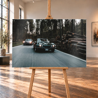 Eine dunkelgrüne 1967 Chevrolet Corvette C2 fährt frontal im Vordergrund einer Waldstraße; links dahinter ist ein dunkelroter 1967 Porsche 911 S Softwindow zu sehen. Die Scheinwerfer leuchten, Fahrer sind sichtbar. Hohe Bäume, gestapelte Baumstämme und Bewegungsunschärfe prägen die Szene; Visualisierung als Alu gebürstet-Wandbild, auf einer Holzstaffelei in einem hellen Galerieraum.