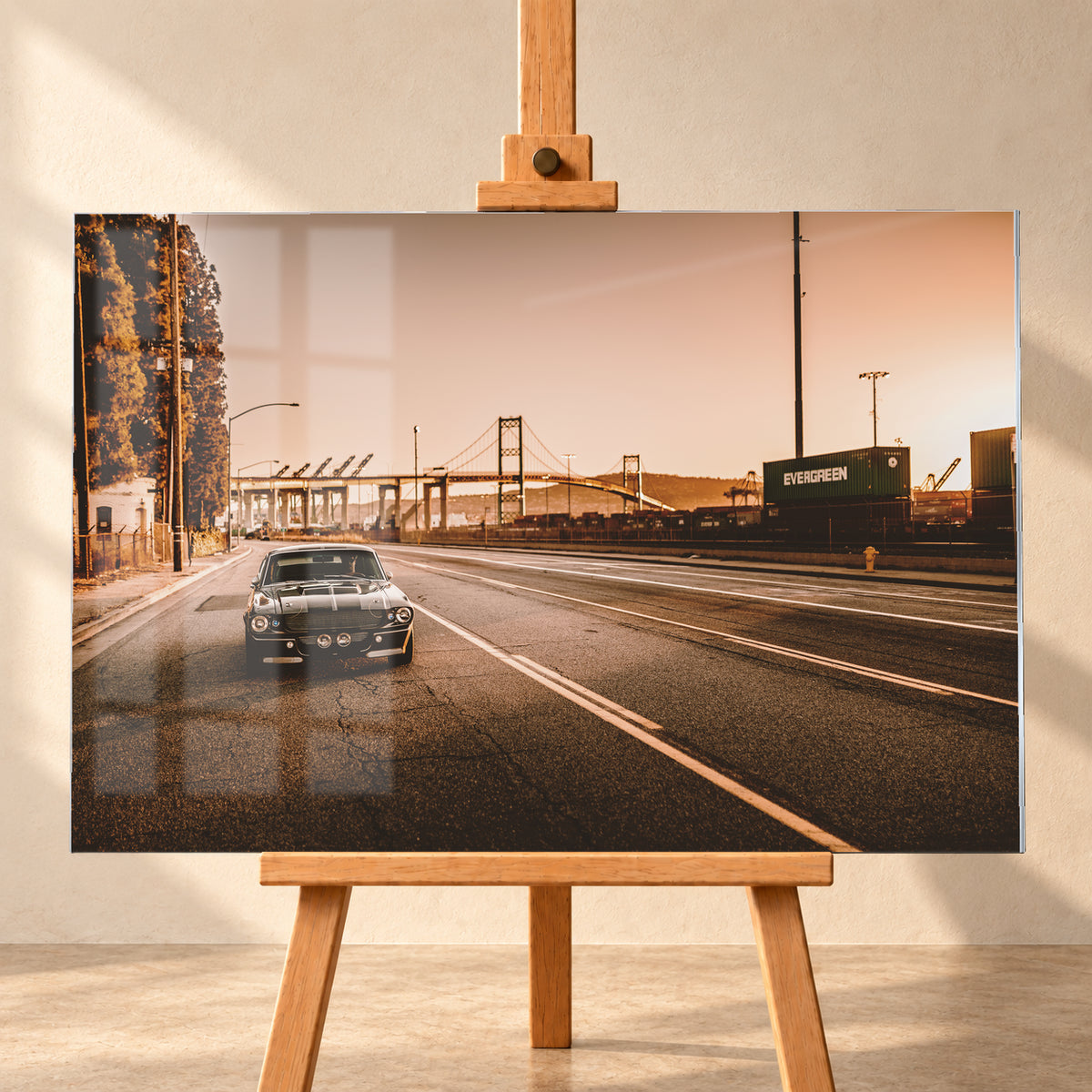 Dunkler klassischer Ford Mustang mit zwei hellen Längsstreifen frontal auf einer breiten Hafenstraße; im Hintergrund stehen eine Hängebrücke, Container und Kräne unter warmem, goldfarbenem Himmel; Visualisierung als Acrylglas-Wandbild, frontal auf einer Holzstaffelei.