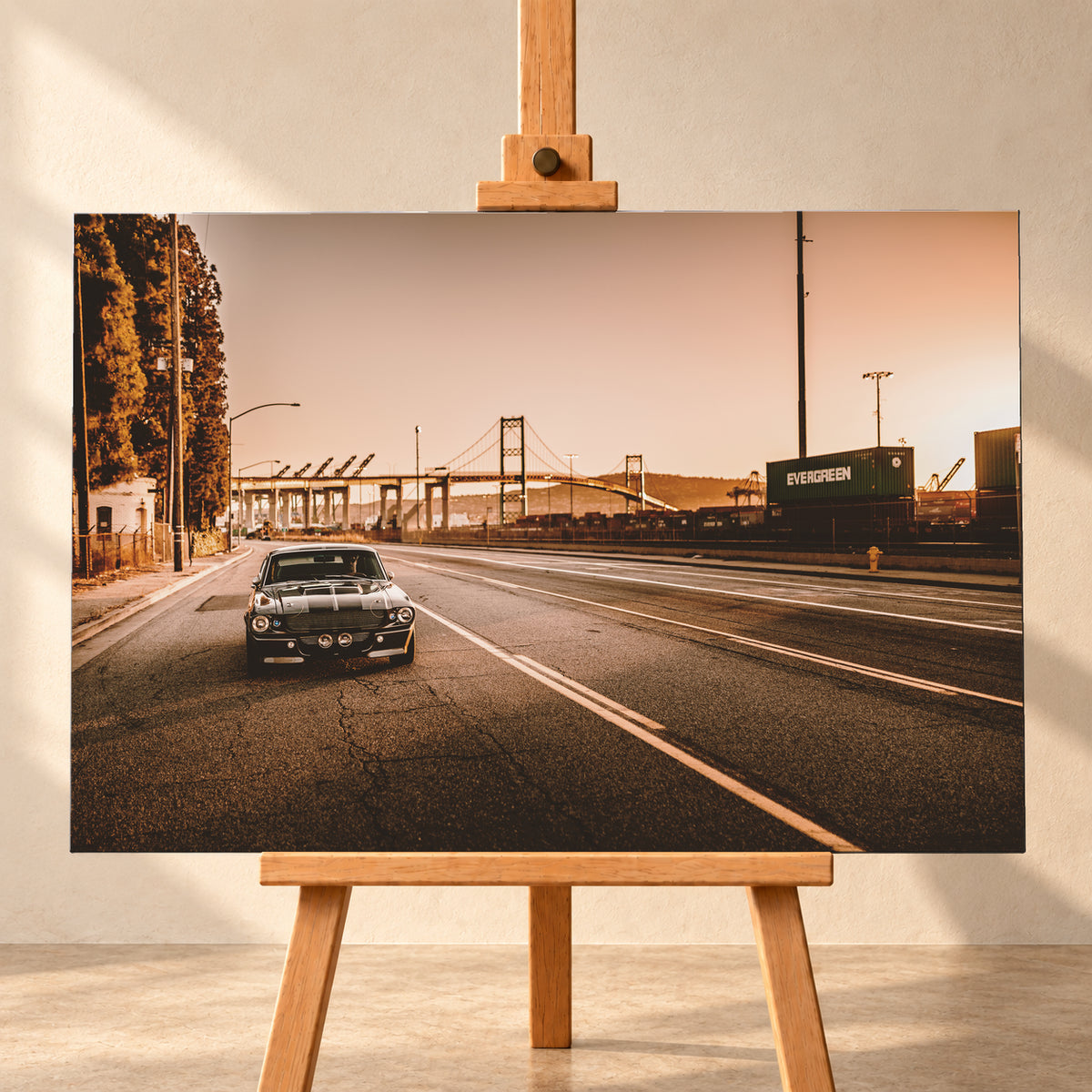 Dunkler klassischer Ford Mustang mit zwei hellen Längsstreifen frontal auf einer breiten Hafenstraße; im Hintergrund stehen eine Hängebrücke, Container und Kräne unter warmem, goldfarbenem Himmel; Visualisierung als Leinwand-Wandbild, frontal auf einer Holzstaffelei.