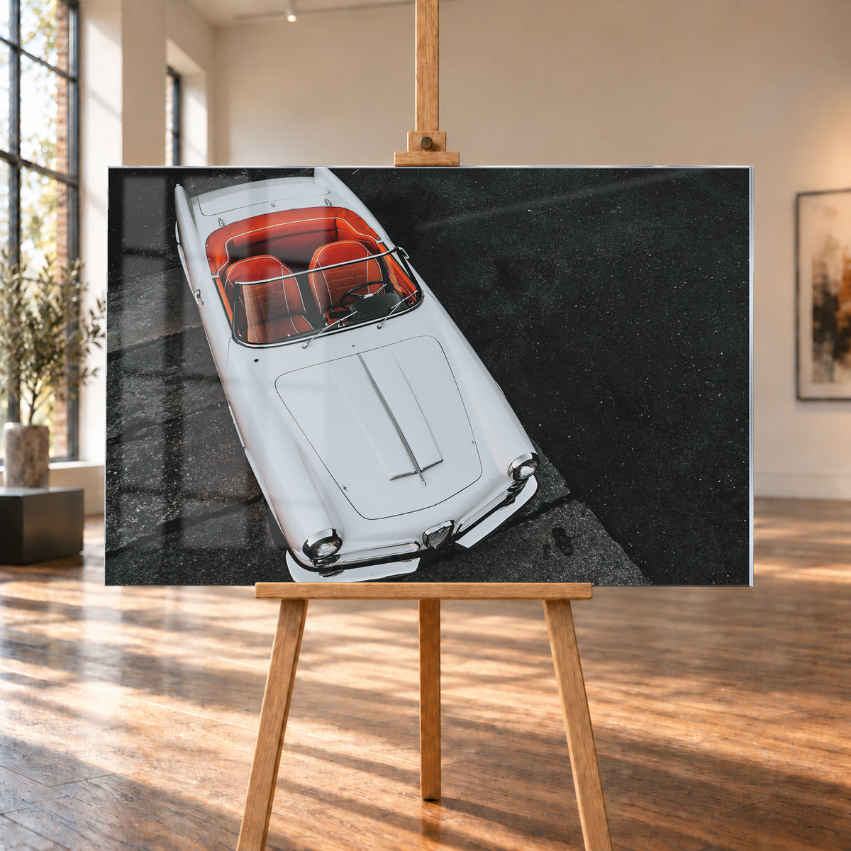 Heller Alfa Romeo 2000 Touring Spider in steiler Aufsicht, diagonal auf dunklem Asphalt; sichtbar sind das offene rot-orange Cockpit, Lenkrad, Windschutzscheibe, lange Motorhaube, runde Frontleuchten und Chromdetails; Visualisierung als Acrylglas-Wandbild, auf einer Holzstaffelei in einem hellen Galerieraum.