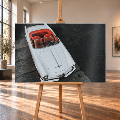 Heller Alfa Romeo 2000 Touring Spider in steiler Aufsicht, diagonal auf dunklem Asphalt; sichtbar sind das offene rot-orange Cockpit, Lenkrad, Windschutzscheibe, lange Motorhaube, runde Frontleuchten und Chromdetails; Visualisierung als Alu gebürstet-Wandbild, auf einer Holzstaffelei in einem hellen Galerieraum.