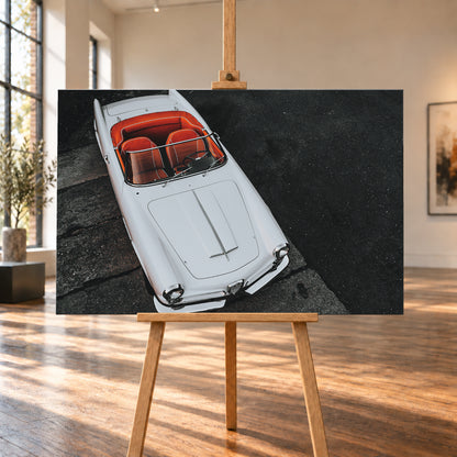 Heller Alfa Romeo 2000 Touring Spider in steiler Aufsicht, diagonal auf dunklem Asphalt; sichtbar sind das offene rot-orange Cockpit, Lenkrad, Windschutzscheibe, lange Motorhaube, runde Frontleuchten und Chromdetails; Visualisierung als Leinwand-Wandbild, auf einer Holzstaffelei in einem hellen Galerieraum.