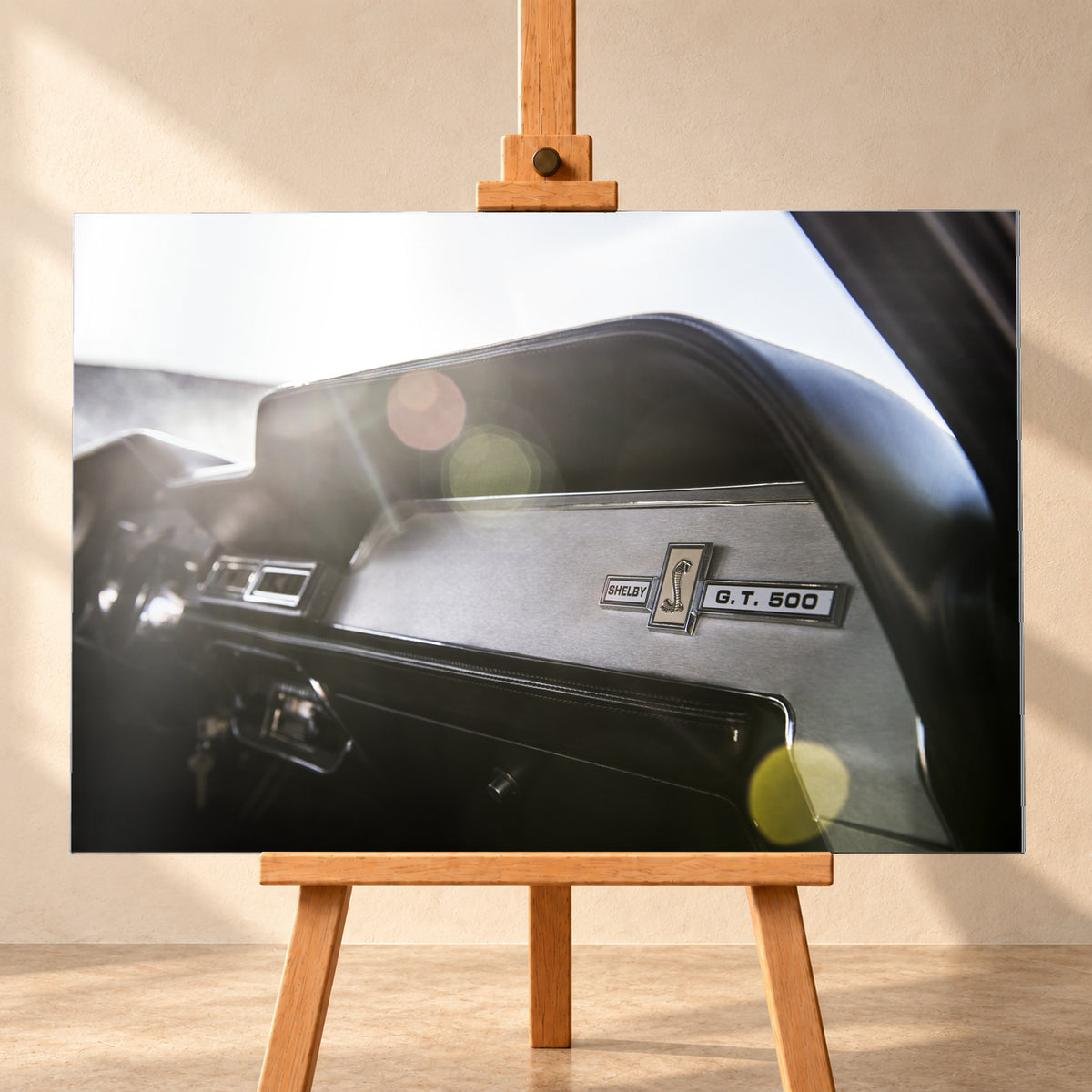 Nahaufnahme des schwarzen Armaturenbretts von Eleanor mit Shelby-, Cobra- und G.T.-500-Emblemen. Helles Gegenlicht fällt von links oben ein und erzeugt grüne, gelbe und rötliche Lichtreflexe; Visualisierung als Alu gebürstet-Wandbild, frontal auf einer Holzstaffelei.