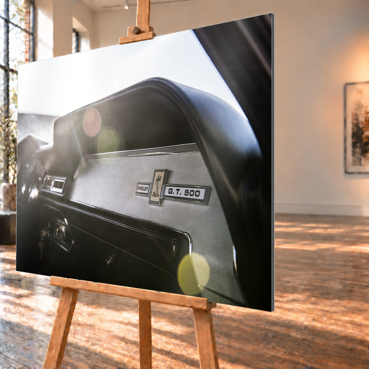 Nahaufnahme des schwarzen Armaturenbretts von Eleanor mit Shelby-, Cobra- und G.T.-500-Emblemen. Helles Gegenlicht fällt von links oben ein und erzeugt grüne, gelbe und rötliche Lichtreflexe; Visualisierung als Alu gebürstet-Wandbild, schräg von der Seite auf einer Holzstaffelei.