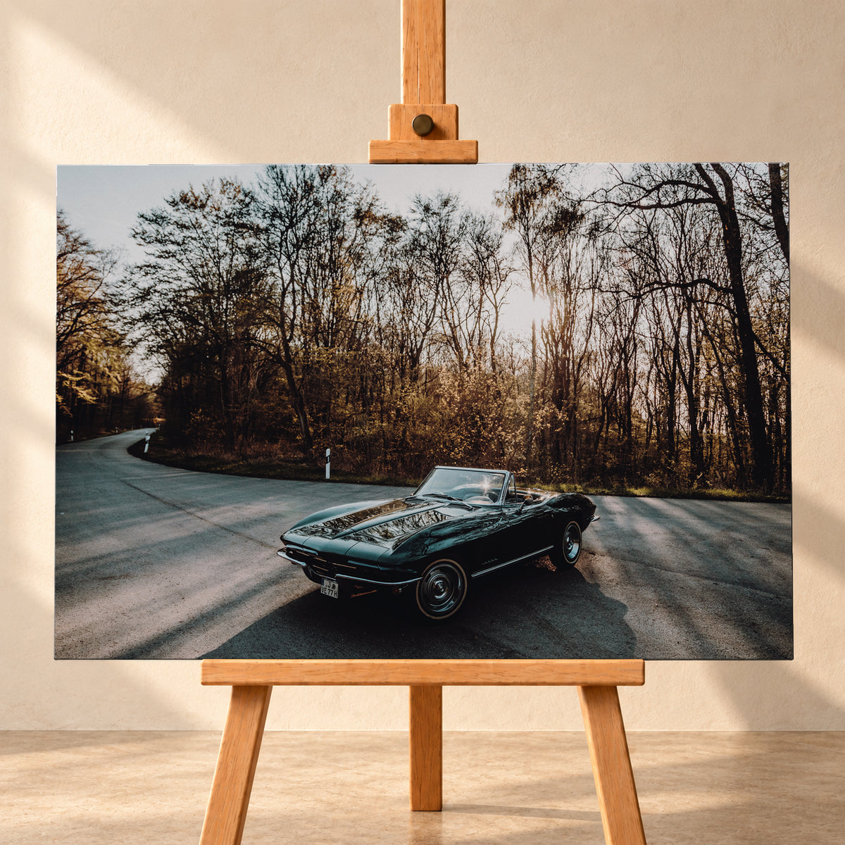 Eine dunkelgrüne 1967 Chevrolet Corvette C2 als offenes Cabriolet in Front-Dreiviertelansicht auf einer kurvigen Waldstraße. Tief stehende Sonne scheint durch kahle Bäume; Gegenlicht und Astspiegelungen liegen auf der Karosserie; Visualisierung als Leinwand-Wandbild, frontal auf einer Holzstaffelei.