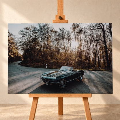 Eine dunkelgrüne 1967 Chevrolet Corvette C2 als offenes Cabriolet in Front-Dreiviertelansicht auf einer kurvigen Waldstraße. Tief stehende Sonne scheint durch kahle Bäume; Gegenlicht und Astspiegelungen liegen auf der Karosserie; Visualisierung als Leinwand-Wandbild, frontal auf einer Holzstaffelei.