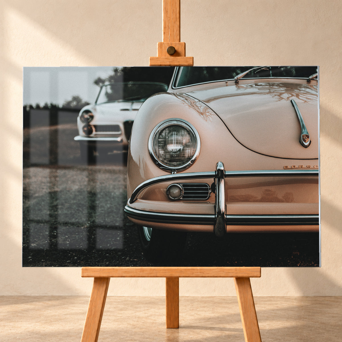 Nahaufnahme der Front eines roséfarbenen Porsche 356 A mit Rundscheinwerfer und Chromstoßfänger rechts; links dahinter steht unscharf ein heller Alfa Romeo 2000 Touring Spider auf dunklem Untergrund unter grauem Himmel; Visualisierung als Acrylglas-Wandbild, frontal auf einer Holzstaffelei.