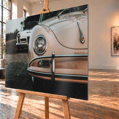 Nahaufnahme der Front eines roséfarbenen Porsche 356 A mit Rundscheinwerfer und Chromstoßfänger rechts; links dahinter steht unscharf ein heller Alfa Romeo 2000 Touring Spider auf dunklem Untergrund unter grauem Himmel; Visualisierung als Alu gebürstet-Wandbild, schräg von der Seite auf einer Holzstaffelei.