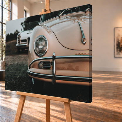 Nahaufnahme der Front eines roséfarbenen Porsche 356 A mit Rundscheinwerfer und Chromstoßfänger rechts; links dahinter steht unscharf ein heller Alfa Romeo 2000 Touring Spider auf dunklem Untergrund unter grauem Himmel; Visualisierung als Leinwand-Wandbild, schräg von der Seite auf einer Holzstaffelei.