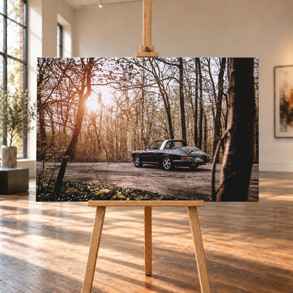 Dunkler 1967 Porsche 911 S Softwindow in seitlicher Heckansicht auf einer unbefestigten Fläche im Wald. Die offene Dachpartie und die helle Bügelzone sind sichtbar, während tiefes Sonnenlicht links durch hohe, spärlich belaubte Bäume fällt; Visualisierung als Leinwand-Wandbild, auf einer Holzstaffelei in einem hellen Galerieraum.
