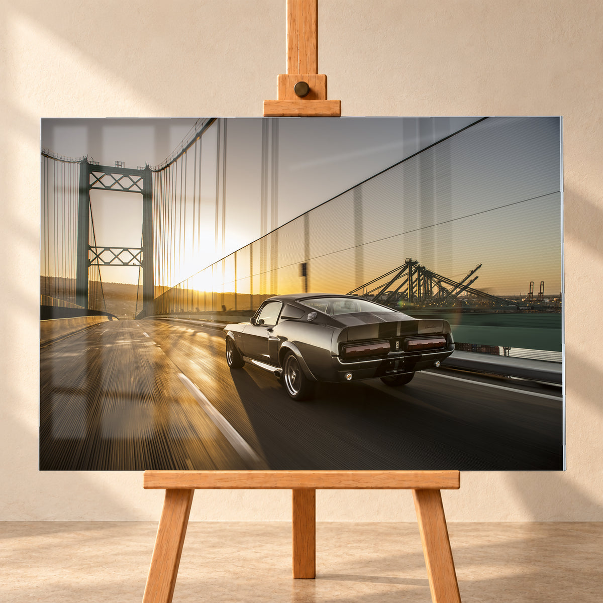 Dunkelgrauer Ford Mustang Fastback in Heck-Dreiviertelansicht auf einer Hängebrücke; goldenes Gegenlicht spiegelt sich auf der Fahrbahn, rechts sind Wasser und Hafenkräne zu sehen; Visualisierung als Acrylglas-Wandbild, frontal auf einer Holzstaffelei.